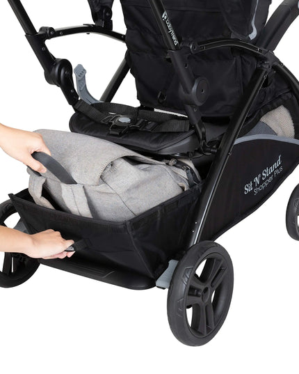 Black and gray stroller with a baby seat being adjusted, featuring 'Sit N Stand' branding.