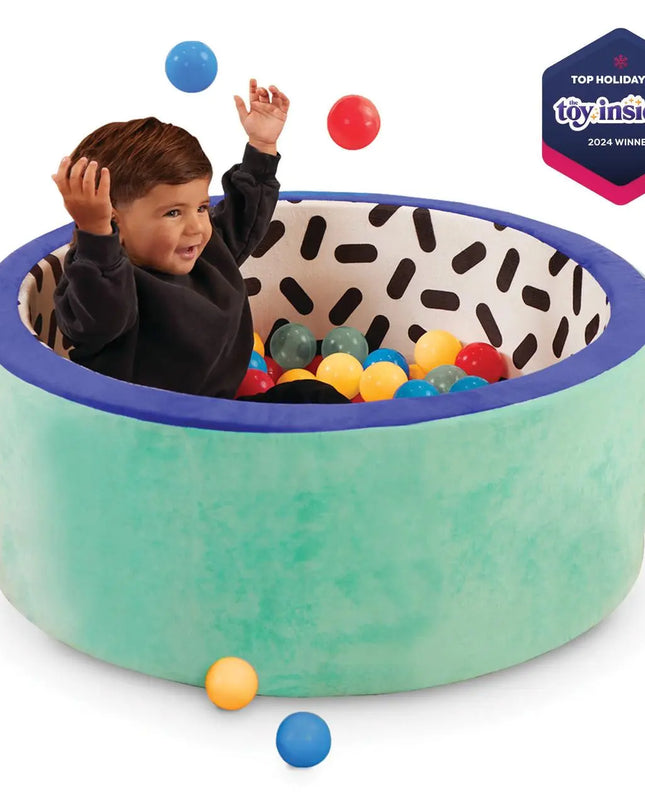 Child playing with colorful balls in a green ball pit, with 'Top Holiday Toy' award from Toy Insider visible.