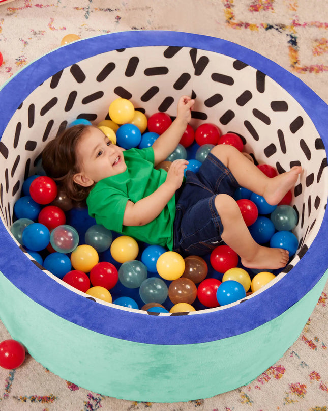 Child playing with colorful balls inside a patterned container on a carpeted floor.