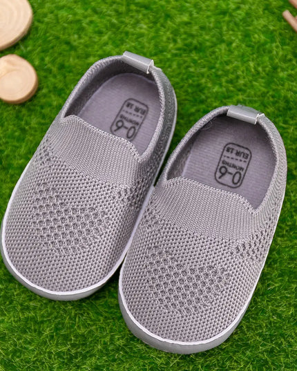 Pair of gray slip-on shoes on a green grass-like surface with wooden blocks and sticks.