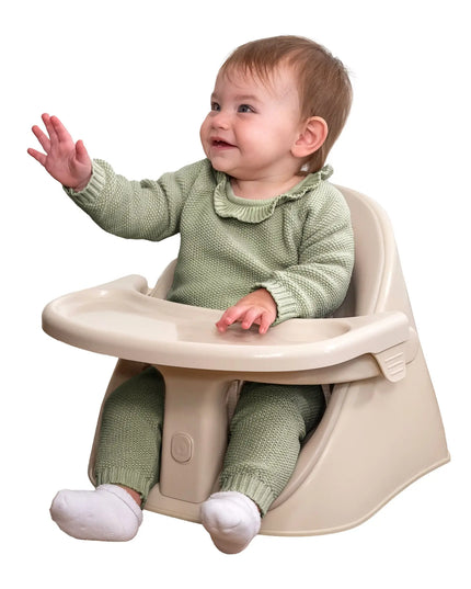 Baby in a green outfit sitting in a beige high chair on a white background