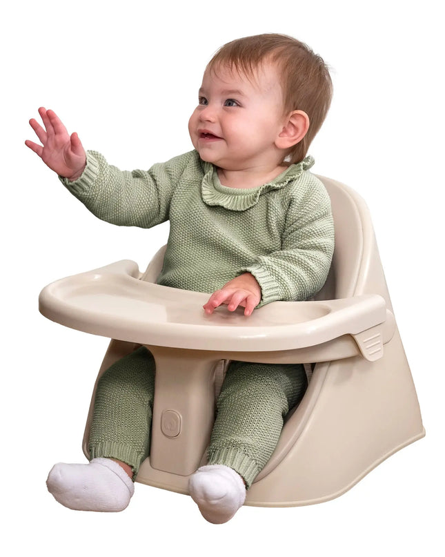 Baby in a green outfit sitting in a beige high chair on a white background