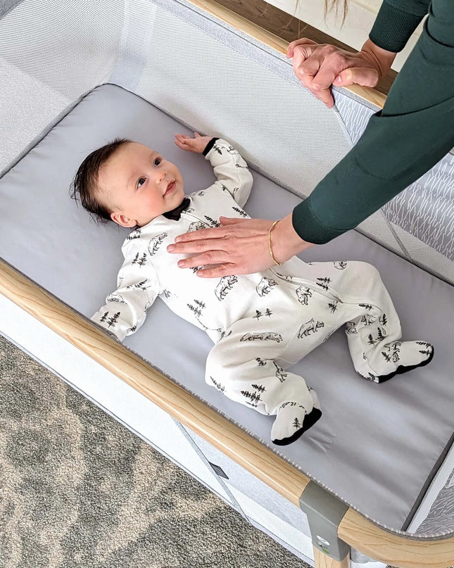 Baby lying in a crib with a person's hand reaching out