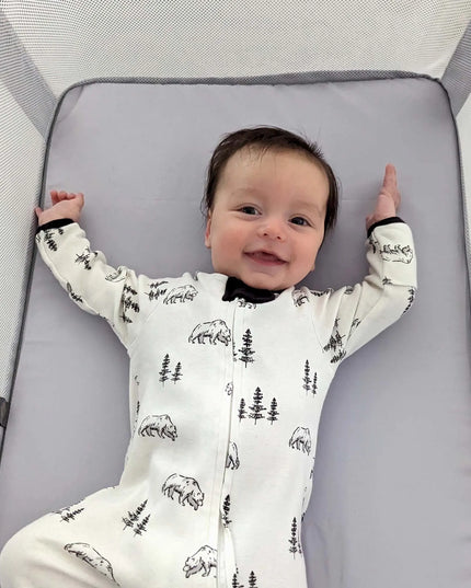 Baby lying on a gray mat with a white onesie featuring black bear and tree patterns.