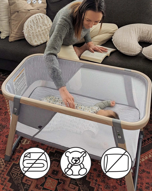 Woman reading a book to a baby in a portable crib on a living room floor.