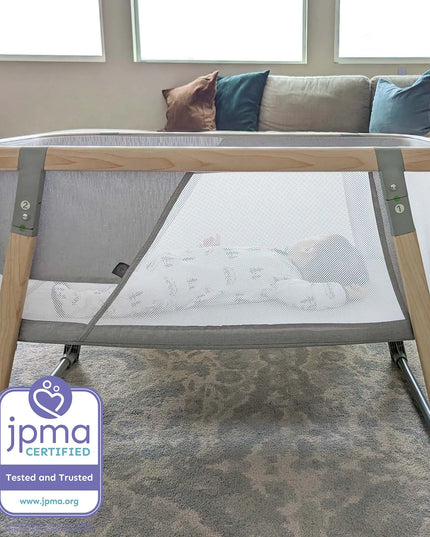 Portable crib in a living room with a JPMA certification label.