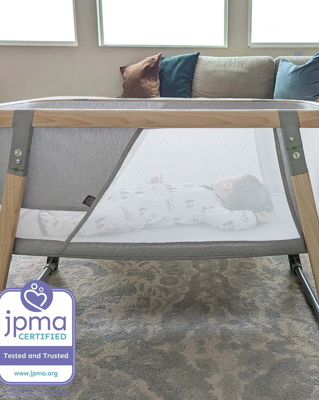 Portable crib in a living room with a JPMA certification label.