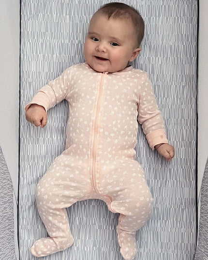 Baby in a pink polka dot onesie lying on a textured surface