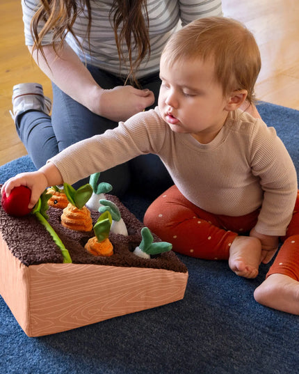 Child playing with a wooden toy garden on a blue rug