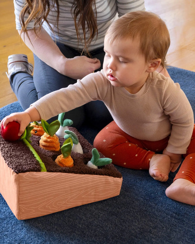 Child playing with a wooden toy garden on a blue rug
