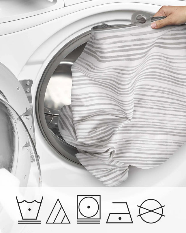 Person loading a striped garment into a washing machine with laundry symbols below.