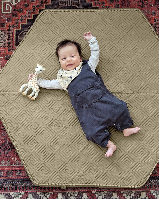 Baby lying on a geometric-patterned mat with a toy on a textured rug