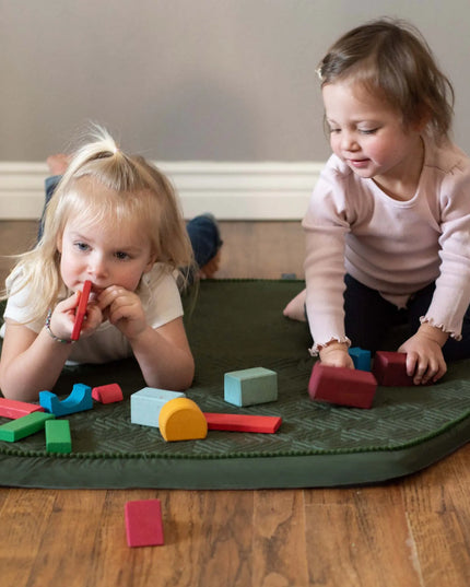 Two young children playing with colorful blocks on a green mat.