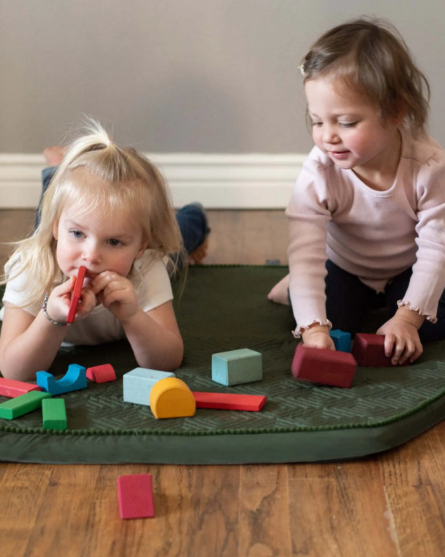 Two young children playing with colorful blocks on a green mat.