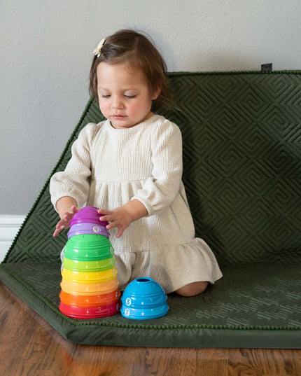 Child playing with colorful stacking toys on a green mat.