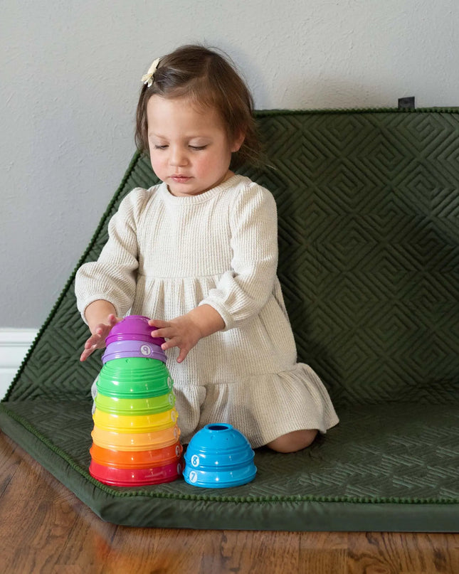 Child playing with colorful stacking toys on a green mat.