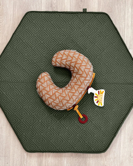 Hexagonal green mat with a patterned neck pillow and toy on a wooden floor.