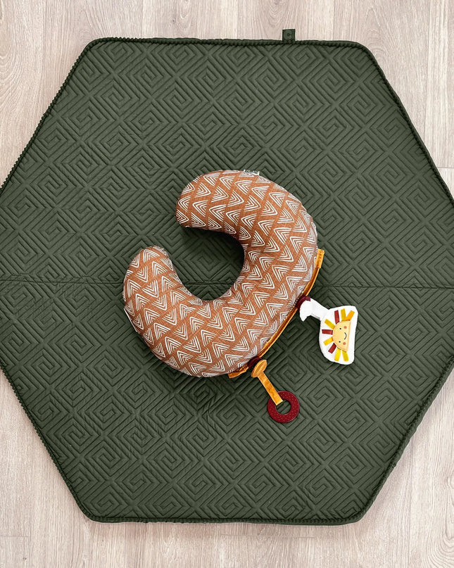 Hexagonal green mat with a patterned neck pillow and toy on a wooden floor.
