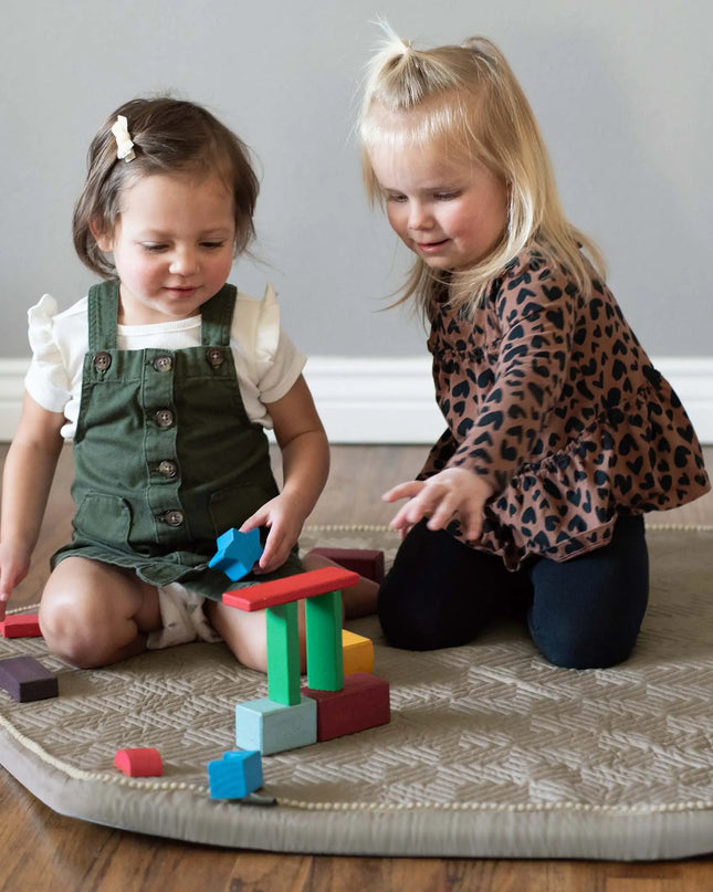 Two young girls playing with colorful building blocks on a rug.