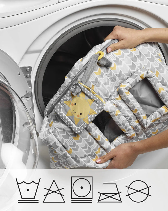 Person holding a baby seat cover with a pattern in front of a washing machine, with laundry symbols at the bottom.
