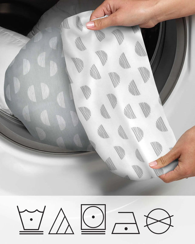 Person holding a patterned fabric in front of an open washing machine with laundry symbols below.