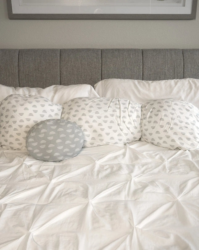 Bed with white bedding and gray patterned pillows against a gray headboard.