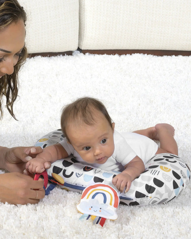 Woman and baby lying on a white carpet with a colorful toy