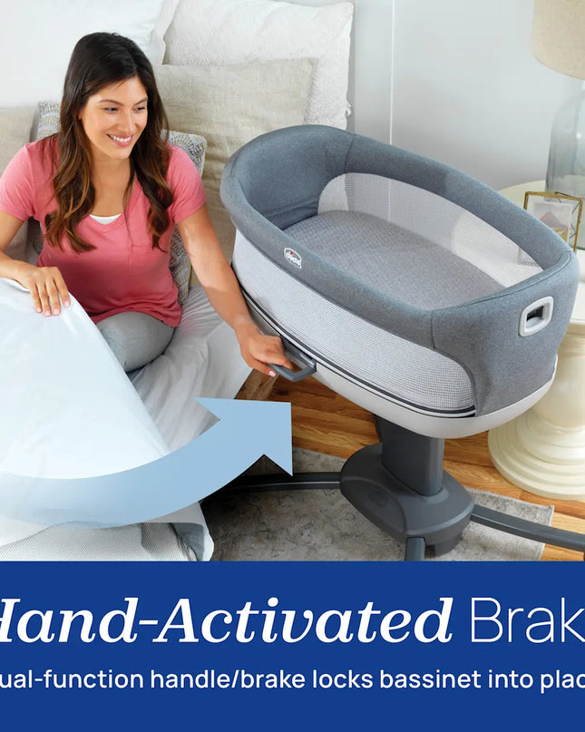 Woman using a gray bassinet with a hand-activated brake system in a bedroom setting.
