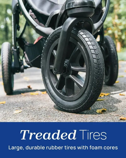 Close-up of a stroller wheel with treaded tires on a road, emphasizing durability.