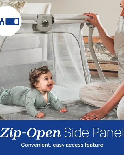 Baby lying in a travel cot with a woman sitting beside it, emphasizing the 'Zip-Open Side Panel' feature.