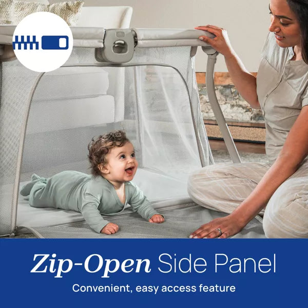 Baby lying in a travel cot with a woman sitting beside it, emphasizing the 'Zip-Open Side Panel' feature.