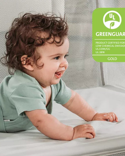 Baby lying on a mattress with a Greenguard Gold certification label in the corner.