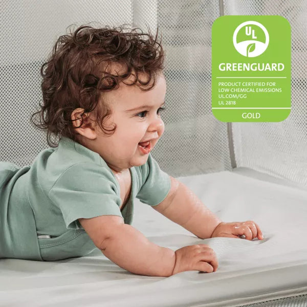 Baby lying on a mattress with a Greenguard Gold certification label in the corner.