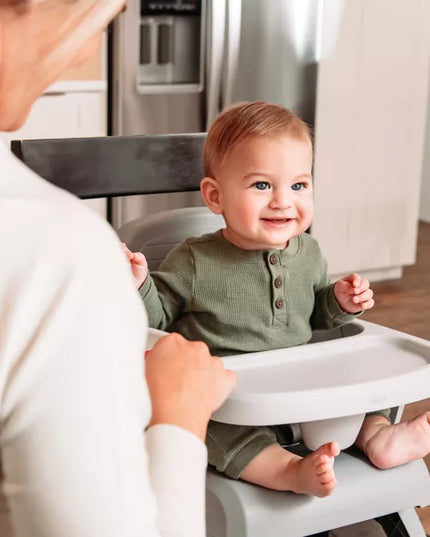 Baby in a high chair with a person assisting, in a kitchen setting