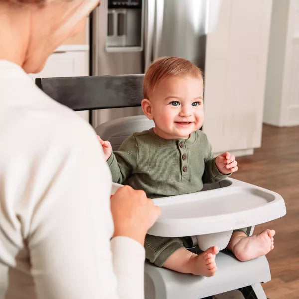 Baby in a high chair with a person assisting, in a kitchen setting