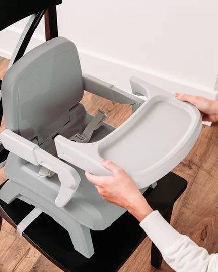 Person attaching a gray baby high chair to a chair on a wooden floor.