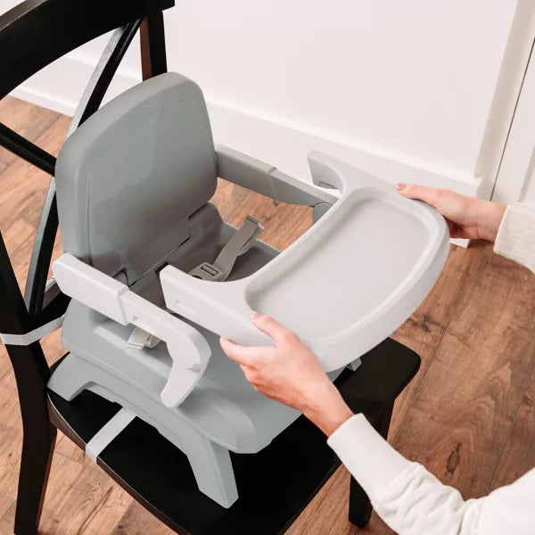 Person attaching a gray baby high chair to a chair on a wooden floor.