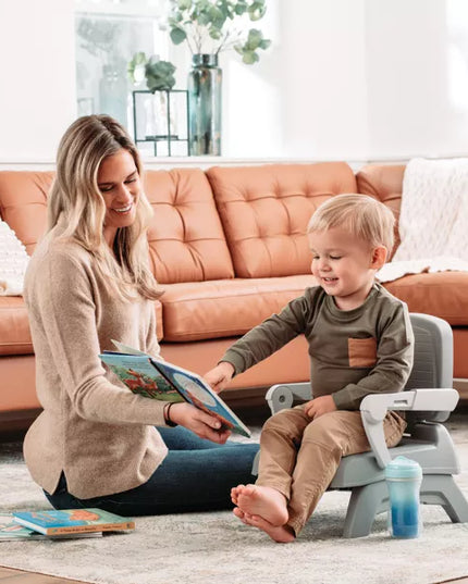 Woman reading a book to a child on a step stool in a living room.