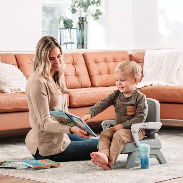 Woman reading a book to a child on a step stool in a living room.