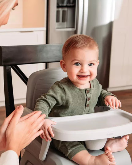 Baby in a high chair smiling in a kitchen setting