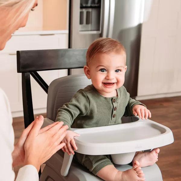 Baby in a high chair smiling in a kitchen setting