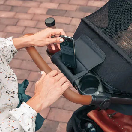 Person using a smartphone in a stroller cup holder on a brick pavement