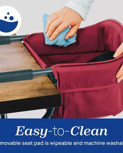 Person cleaning a maroon high chair with a blue cloth on a light gray background.