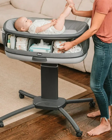 Baby in a portable changing table with diapers and a woman assisting.