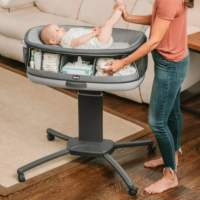 Baby in a portable changing table with diapers and a woman assisting.