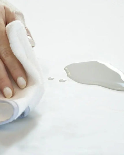 Hand applying a white cream to a small applicator on a light background