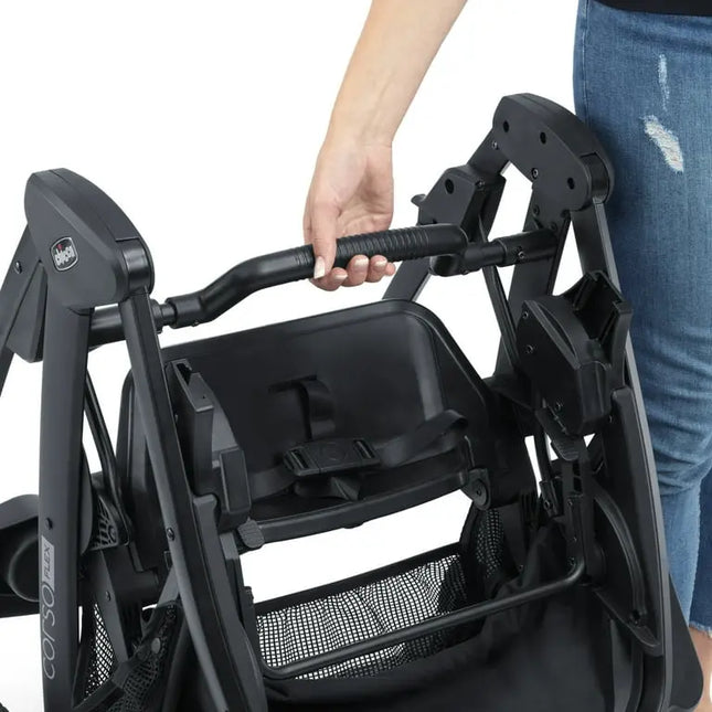 Close-up of a black stroller with a hand gripping the handle, on a white background.