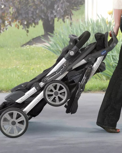 Person pushing a black and silver stroller outdoors on a path.