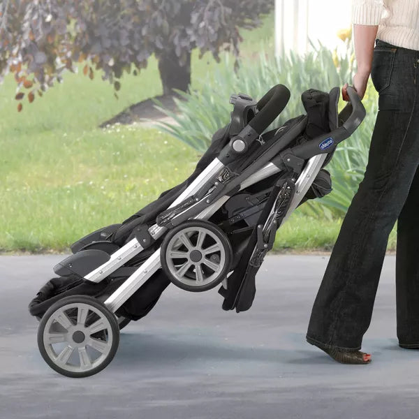 Person pushing a black and silver stroller outdoors on a path.