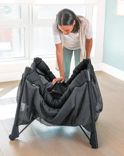 Woman assembling a black baby bouncer in a room with large windows.